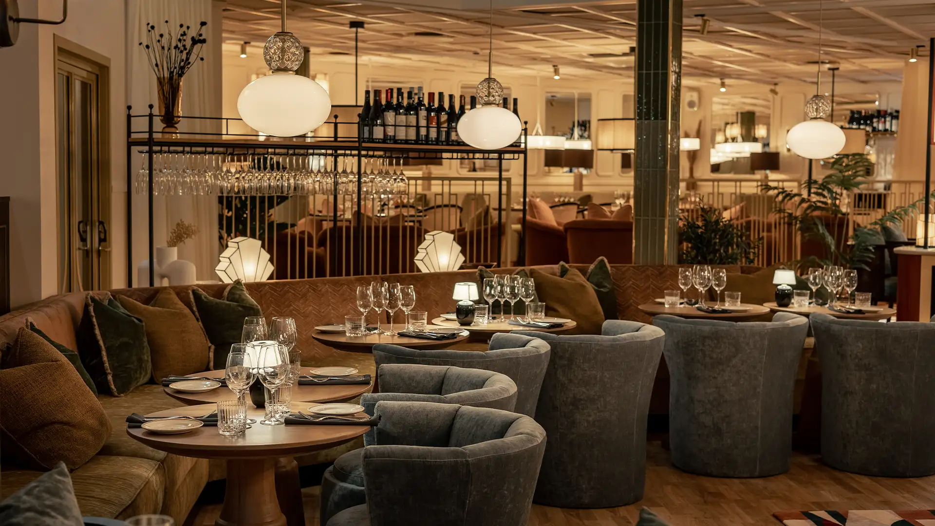 Archies-goteborg-restauranger Dukat hörnbord i Archie’s restaurang med sammetspuffar, vinflaskor och mjuk belysning i varm miljö.