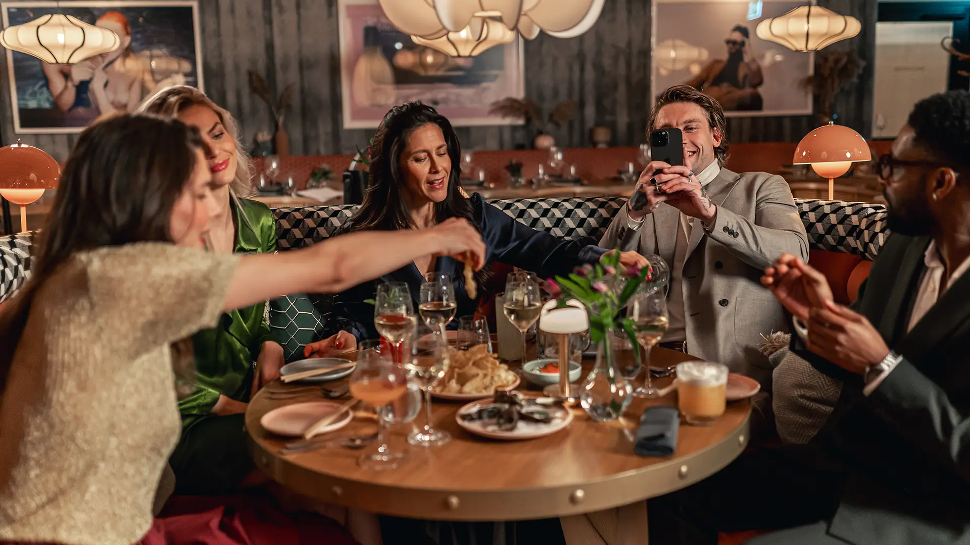 Asian-fusion-restaurang-goteborg Ett sällskap skrattar och delar smårätter vid ett rundbord i en livlig restaurangmiljö med asian fusion-tema.