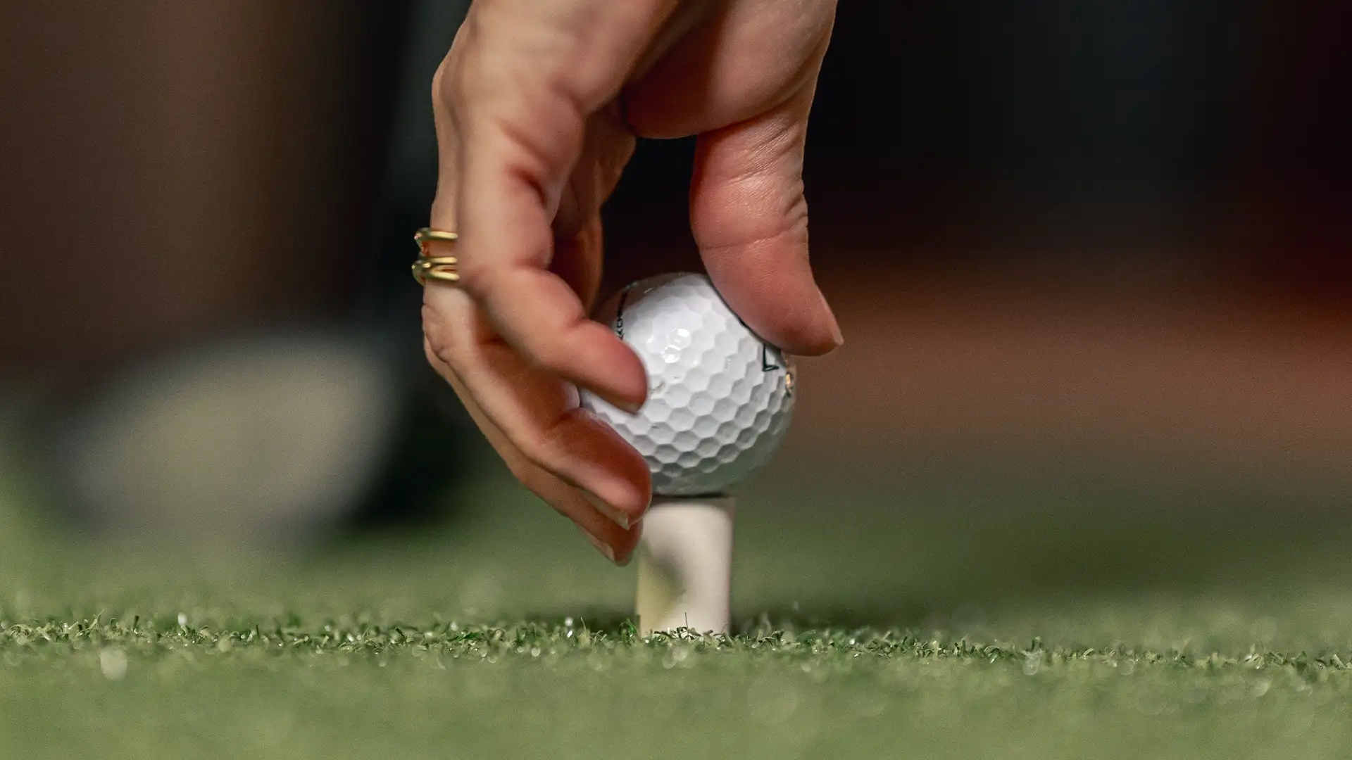 Golf-simulator-goteborg En hand placerar en golfboll på en peg på konstgräs.