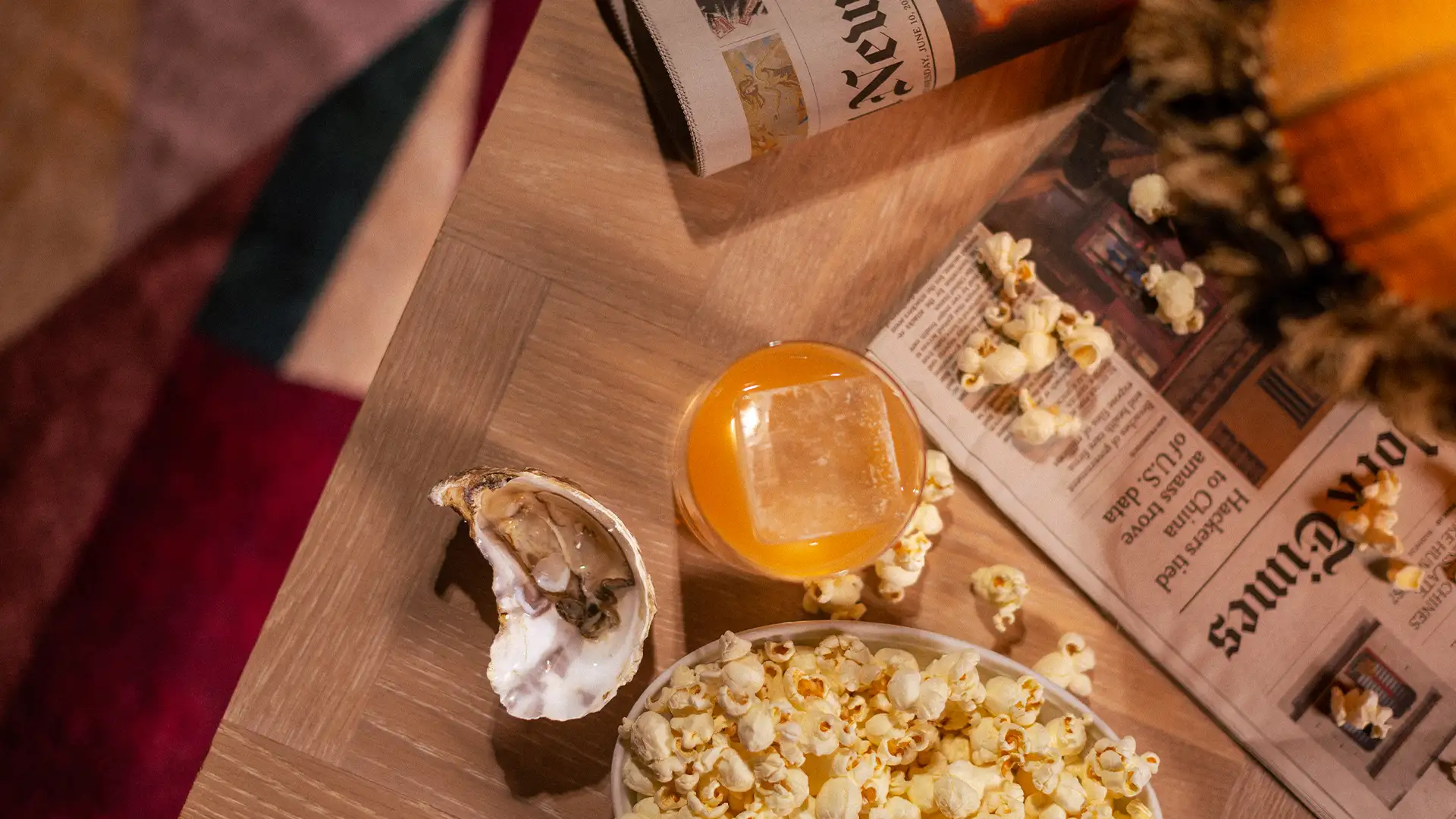 archies-goteborg Närbild på ett träbord med popcorn, ostron, drink med is och dagstidningar i mjukt ljus.