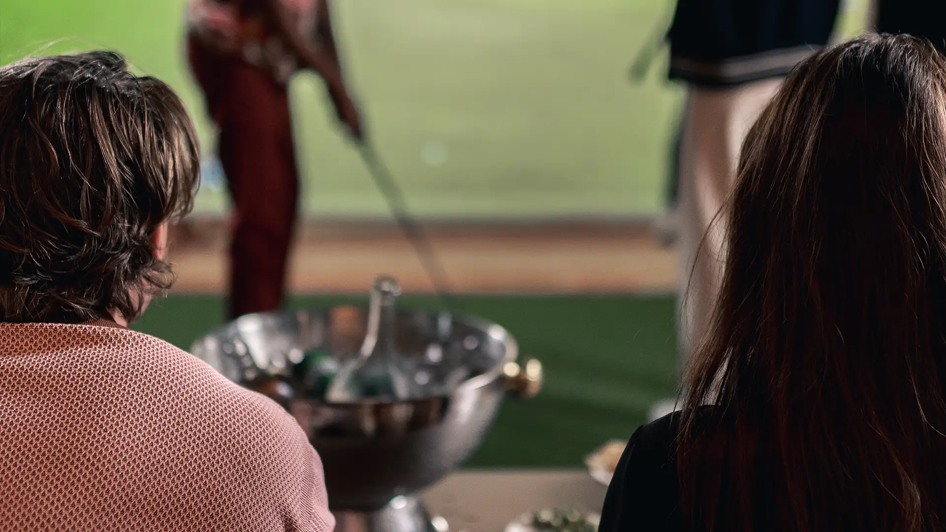 golf-med-servering Personer tittar på medans en spelar golfsimulator, med dryck serverad i ishink.