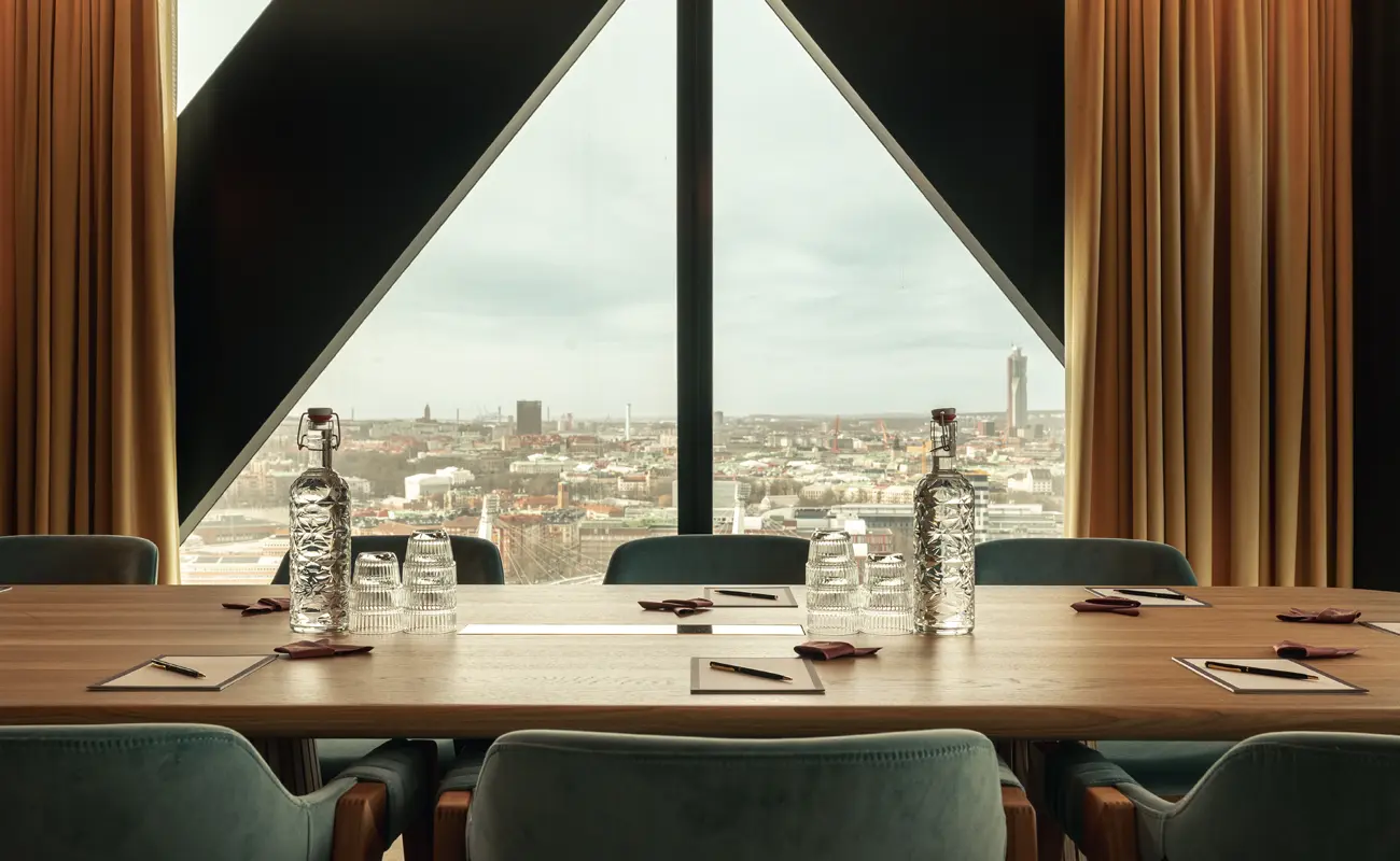 konferensrum-utsikt-jacyz-goteborg Ett elegant konferensrum på Jacy’z med panoramavy över Göteborg, uppdukat med anteckningsblock, pennor, glas och karaffer på ett stort träbord.