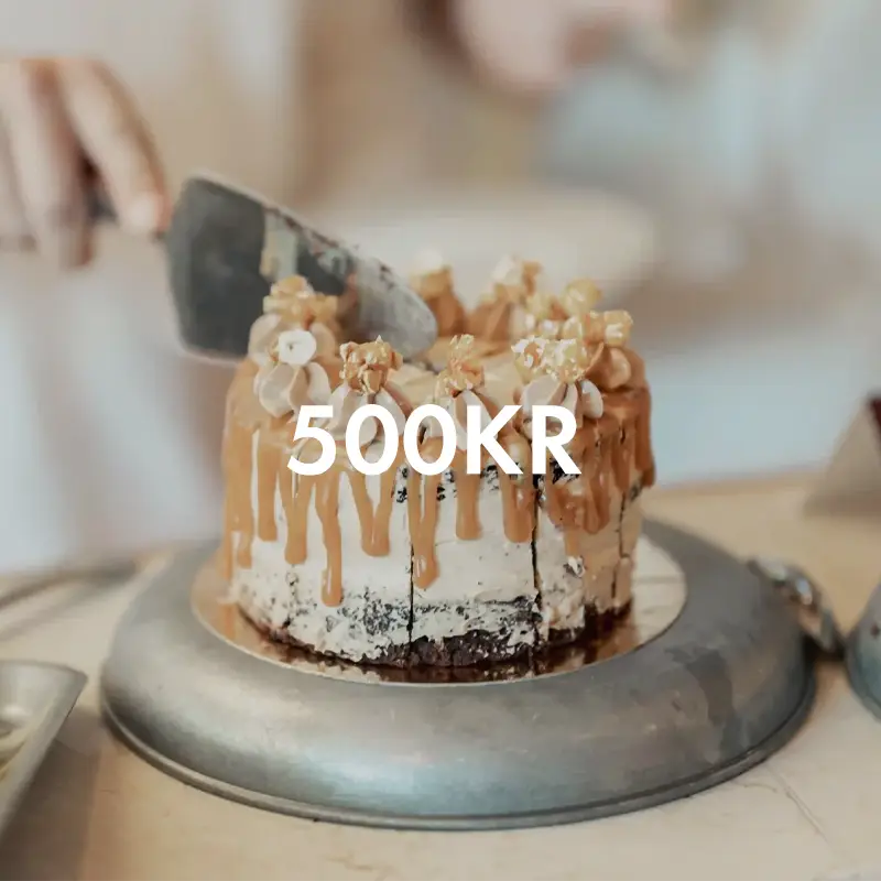 En hand som skär med i en lyxig karamelltårta toppad med popcorn, med texten "500 KR" över bilden.